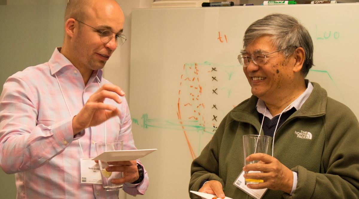 Two men wearing name tags and holding drinks laugh together.